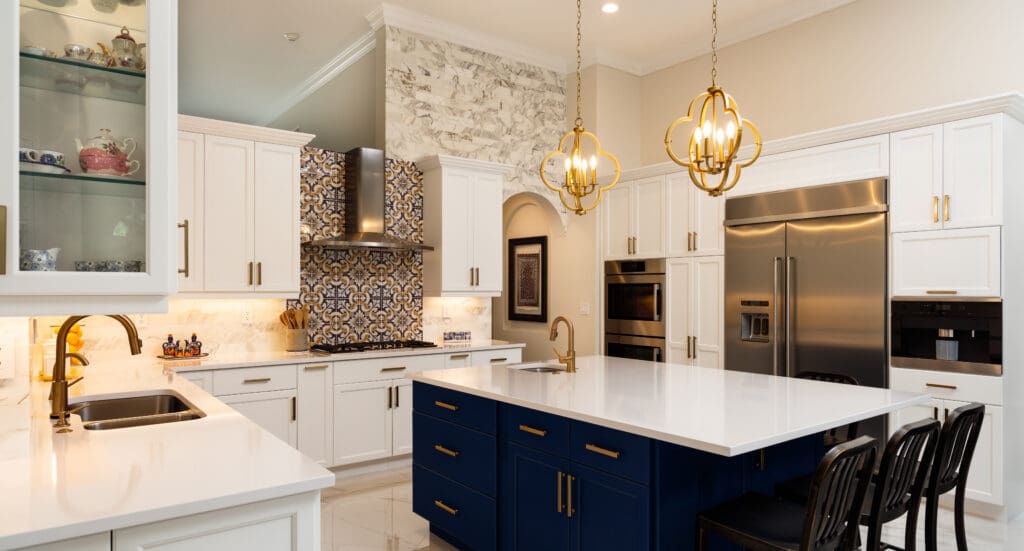 Modern kitchen extensions feature white cabinets, a blue island, gold pendant lights, stainless steel appliances, patterned tile backsplash, and marble accents. Three black chairs sit at the island in this bright and elegant space.