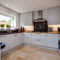 Modern kitchen extensions feature white cabinets, black countertops, stainless steel appliances, and a hood over the stove. A window with potted plants, tiled floor, and under-cabinet lighting create a bright, clean space.