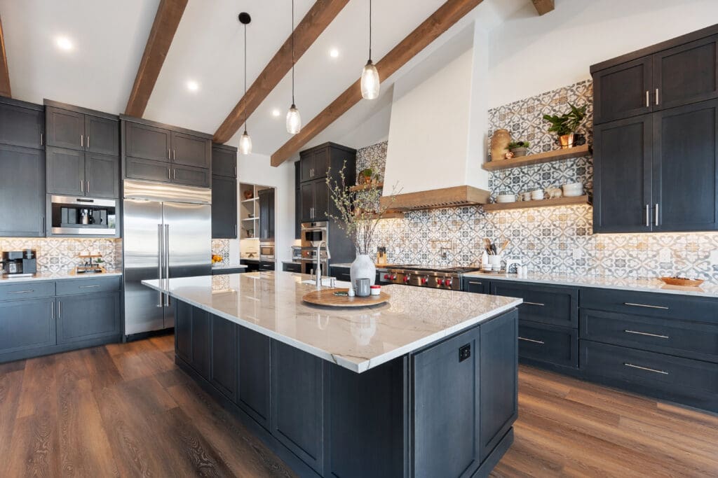 Modern kitchen with dark cabinetry, stainless steel appliances, marble island countertop, patterned tile backsplash, exposed wood ceiling beams, wood flooring, and decorative items—perfect inspiration for stylish kitchen extensions.